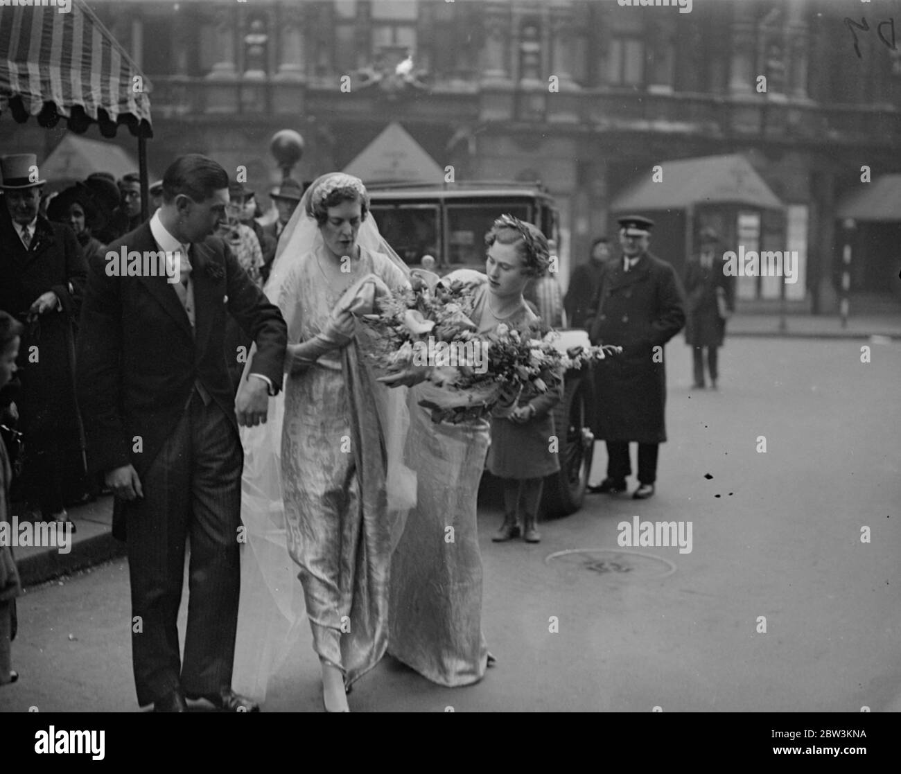 Brautprozession über Langham Platz nach allen Seelen Hochzeit. Nach ihrer Hochzeit in All Souls Church, Langham Place, W, Capital Victor Paley der Gewehrbrigade, und seine Braut, forma Miss Susan Paine, ging über die Straße mit ihrem Gefolge zum Langham Hotel, wo der Empfang stattfand. Foto zeigt, ein Brautjungfer sdjusting der Braut ' s Zug, als sie über die Straße ging mit dem Bräutigam und der Gefolge. 14. April 1936 Stockfoto