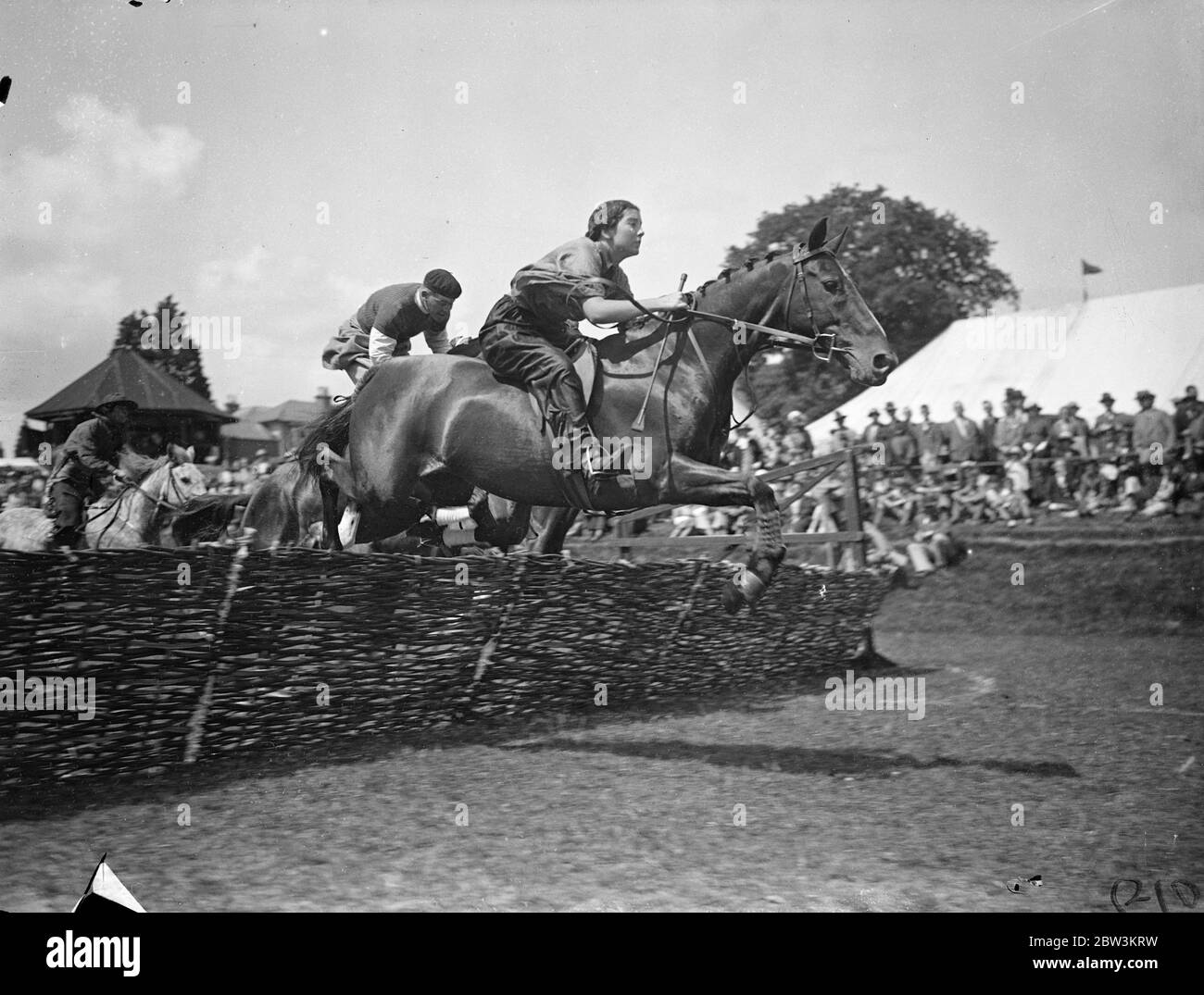 Ausgefallenes Kleid Steeplechase im Haywards Heath Gymkhana! Foto zeigt: Tragen ausgefallene Kostüm, Miss Sheila Price nimmt ihr Pony Polymint über die Hürden in einem herrlichen Sprung von Herrn gefolgt. G . A . Preis während des Kostüm-Rennen bei der Haywards Heath Gartenbaugesellschaft ' s Sommer-Show in Victoria Park, Haywards Heath, Sussex. Im Rennen, das war eine der Neuheiten der berittenen Veranstaltungen in der Show, alle Fahrer hatten volle Phantasie Kleid für die Hindernislauf tragen. Juli 1936 Stockfoto
