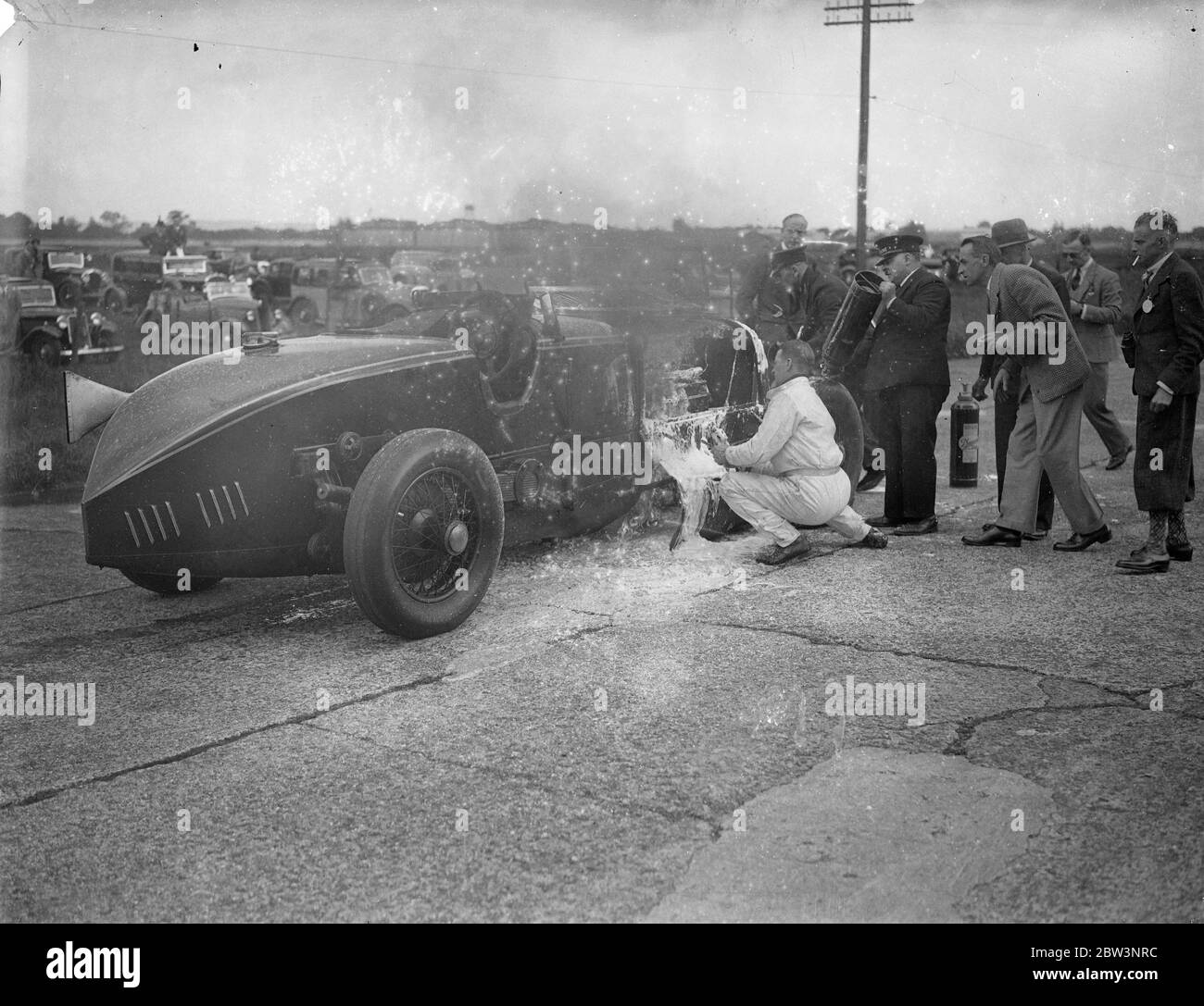 Auto explodiert und bricht in Flammen in Big Race in Brooklands The Leyland - Thomas Auto von R angetrieben. J . Munday in der Gold Trophy Race, die Chief Event bei der Brooklands Whit Montag Sitzung, explodierte und in Flammen mit hoher Geschwindigkeit. Mit dem Auto lodern, Munday fuhr auf für etwa eine halbe Meile, bis er Gangway erreicht, wo versucht wurde, das Feuer zu löschen. Munday half im Kampf. Foto zeigt : R . J . Munday (in weiß) helfen, die Flammen seines lodernden Autos zu bekämpfen. Juni 1936 Stockfoto