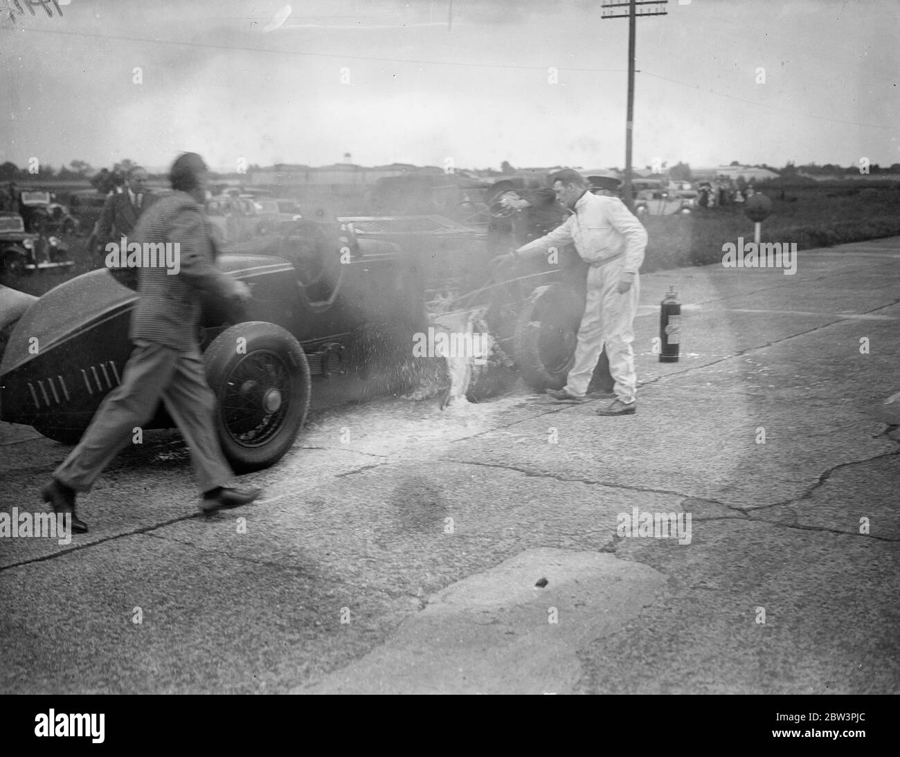 Auto explodiert und bricht in Flammen in Big Race in Brooklands The Leyland - Thomas Auto von R angetrieben. J . Munday in der Gold Trophy Race, die Chief Event bei der Brooklands Whit Montag Sitzung, explodierte und in Flammen mit hoher Geschwindigkeit. Mit dem Auto lodern, Munday fuhr auf für etwa eine halbe Meile, bis er Gangway erreicht, wo versucht wurde, das Feuer zu löschen. Munday half im Kampf. Foto zeigt : R . J . Munday (in weiß) helfen, die Flammen seines lodernden Autos zu bekämpfen. Juni 1936 Stockfoto