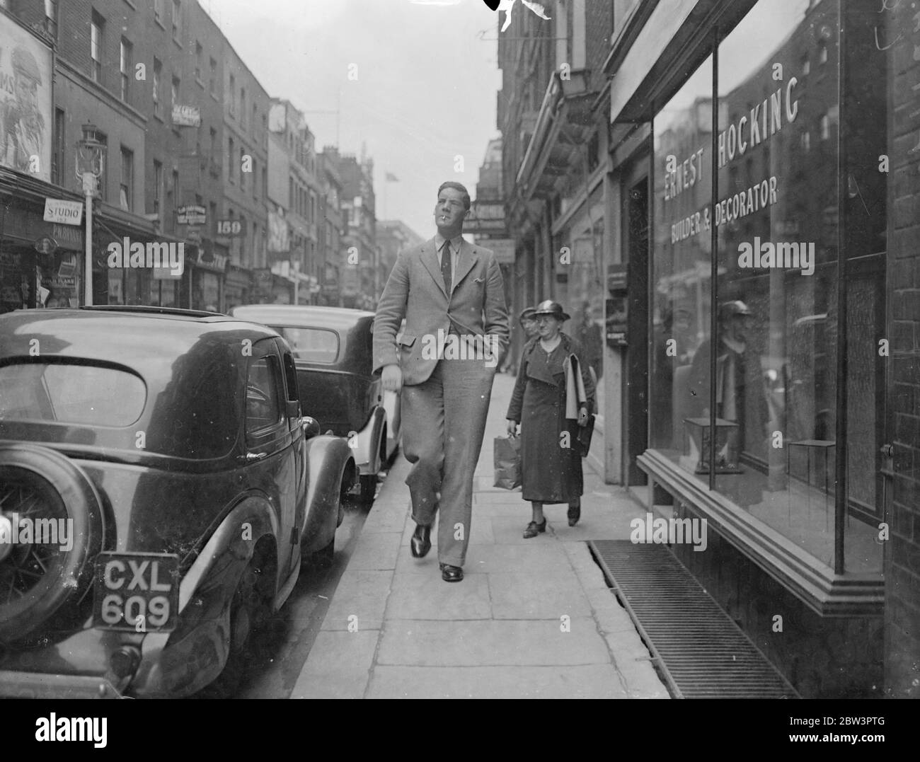 Mann 7 Fuß 6 in, groß, um höchste ' Engel ' zu sein. Stehen 7 ft 6 in und mit einem Gewicht von 24 Stein, Herr W Olding, der behauptet, der höchste Mann in England zu sein, Wird einer der größten "Engel" jemals bekannt, wenn er spielt St Michael an der PAgent of Tudor Days im Hurlingham Club am 23. Juli von ihm inszeniert werden "Waifs and Strays" Gesellschaft . Zwanzig Meter Stoff sind erforderlich, um ihn zu drapieren, und der Schneider musste eine Treppe Leiter zu montieren, um seine massiven Schultern zu erreichen. Foto zeigt Herrn W. Olding Zwerge vorbeigehen, wie er im West End geht. 10 Juli 1936 Stockfoto