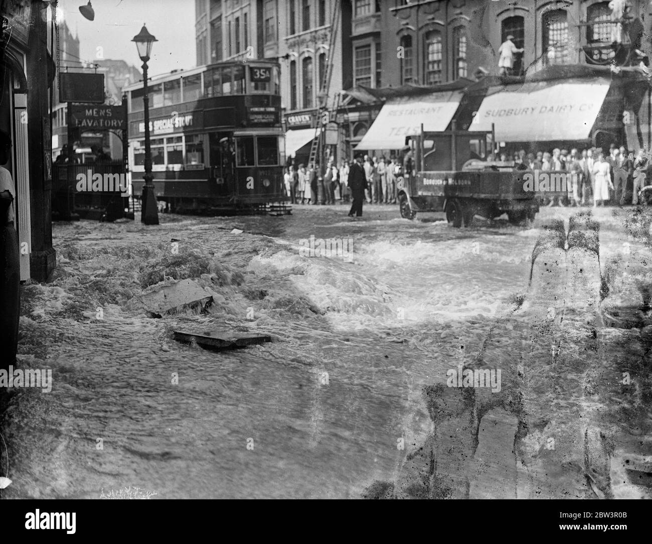 Theobald ' s Straße in einen Fluss durch Wasser Haupt Burst. Theobald ' s Road wurde von Bloomsbury nach Holborn durch einen großen Wasserhauptplatzen am Bloomsbury Ende überschwemmt. Die Oberfläche der Fahrbahn war schwer beschädigt und der Verkehr schickte Duschen von Spray, wie es durch das Wasser in London für eine lange Zeit bekannt spritzte. Foto zeigt, Wasser spuckt aus dem riesigen Loch an der Szene des Bursts. 17 Juni 1936 Stockfoto
