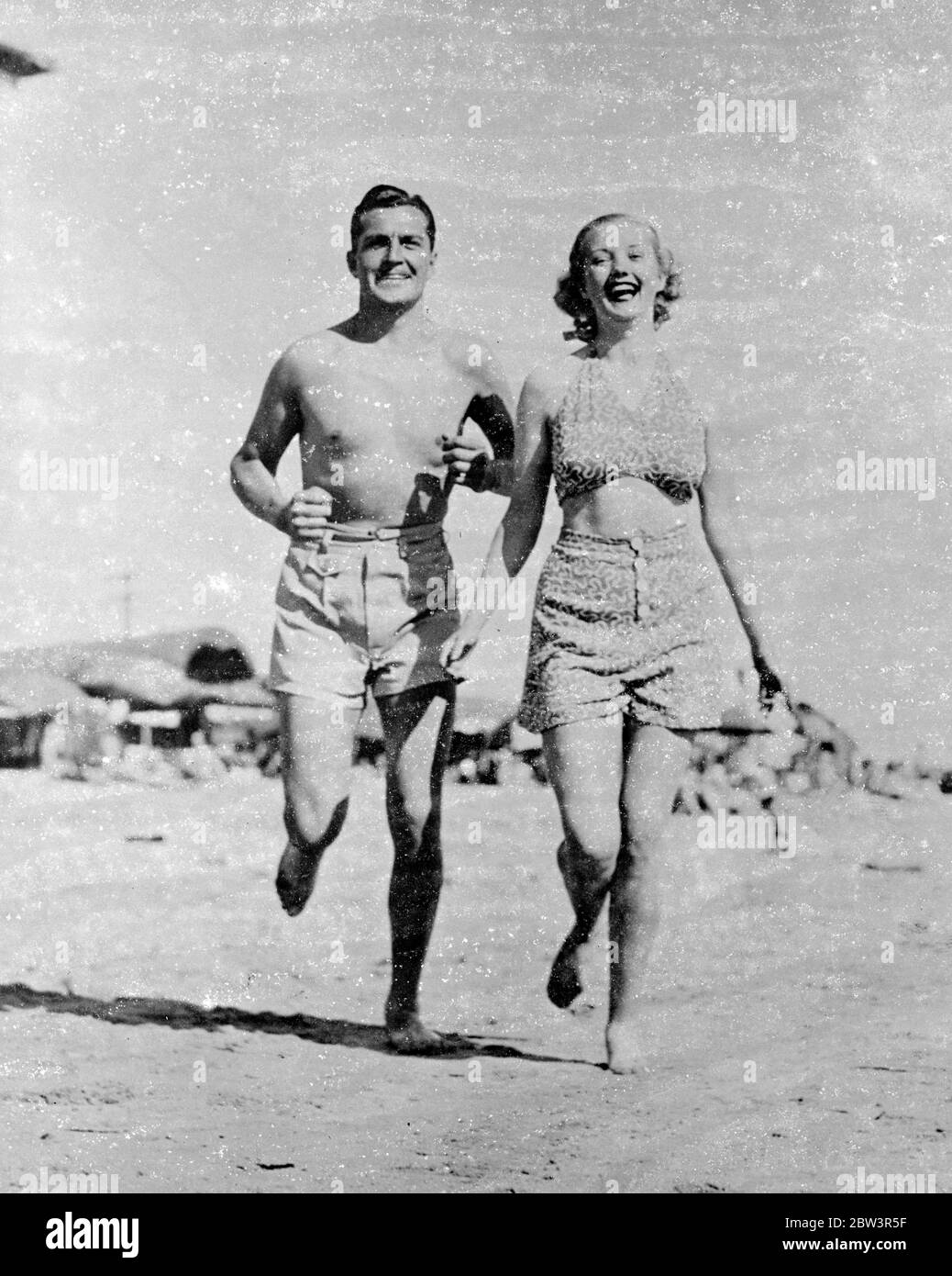Toben am Strand. Kent Taylor und Phyllis Brooks, die Hollywood-Filmspieler, machen einen Run am Strand von Santa Monica, Kalifornien. Mai 1936 Stockfoto