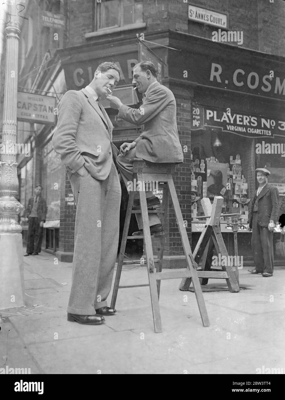 Mann 7 Fuß 6 in, groß, um höchste ' Engel ' zu sein. Stehen 7 ft 6 in und mit einem Gewicht von 24 Stein, Herr W Olding, der behauptet, der höchste Mann in England zu sein, Wird einer der größten "Engel" jemals bekannt, wenn er spielt St Michael an der PAgent of Tudor Days im Hurlingham Club am 23. Juli von ihm inszeniert werden "Waifs and Strays" Gesellschaft . Zwanzig Meter Stoff sind erforderlich, um ihn zu drapieren, und der Schneider musste eine Treppe Leiter zu montieren, um seine massiven Schultern zu erreichen. Foto zeigt Herrn W Olding, der ein Licht von einem Passanten annimmt, bei dem er Zwerge zeigt, wenn er im West End spazieren geht. 10 Juli 1936 Stockfoto