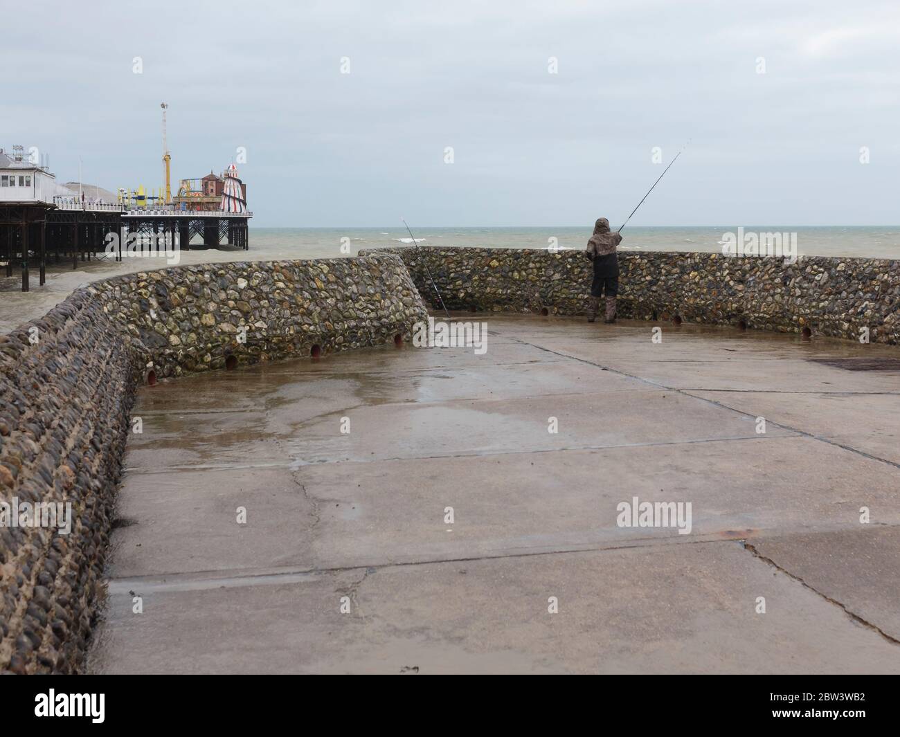 Ein Mann, der bei stürmischem Wetter am Brighton Palace Pier von einem Groyne aus angeln muss, Brighton, England Stockfoto