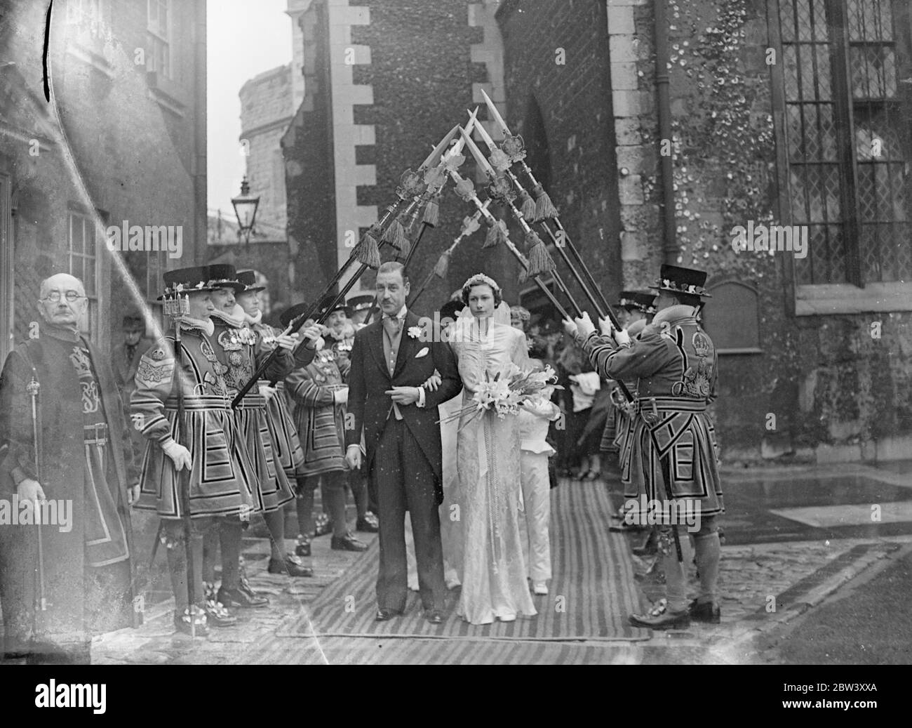 Tochter von Lord Milne heiratet am Turm. Der Hon, Joan Milne Tochter von Lord Milne, der Vollzugsbeamter des Tower of London, war mit Herrn JH Rutland in der historischen Kirche von St. Peter und Vincula im Turm verheiratet. Nach der Zeremonie ging die Braut und der Bräutigam über das Königshaus, das gegenüber der Kirche steht, zum Empfang. Das Haus, das in Heinrich VIII. Zeit für den Leutnant des Turms gebaut wurde, wird jetzt als Residenz für den Vollzugsbeamter gehalten. Foto zeigt, die Braut und Bräutigam vorbei an der Ehrenwache der Yeoman Arders mit Halbbarden. 16 März 1937 Stockfoto