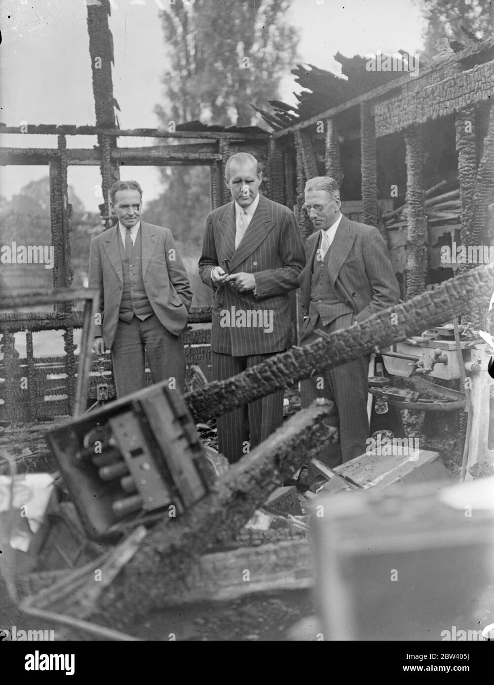 Blinder MP bei St. Dunstans Feuer. Frühmorgendliche Flammen zerstörten zwei Gebäude. Kapitän Sir Ian Fraser, der blinde Abgeordnete und Vorsitzende von St. Dunstan [später bekannt als Blind Veterans UK] wurde durch die Feuerglocken geweckt, kam von seinem Haus im Regent's Park, um festzustellen, dass die beiden Holzgebäude, die an St. Dunstan's angeschlossen waren, in Flammen standen. Die beteiligten Schuppen waren zwei Holzgebäude, die als Tischlerei und Ingenieursmaschinenwerkstatt genutzt wurden. Zwei Nachtwächter das Feuer in Schach, bis die Brigade eintraf. Foto zeigt: captain Sir Ian Fraser (Mitte) zwischen den Ruinen der ausgebrannten Gebäude, mit W. G. Askew und The Secret Stockfoto