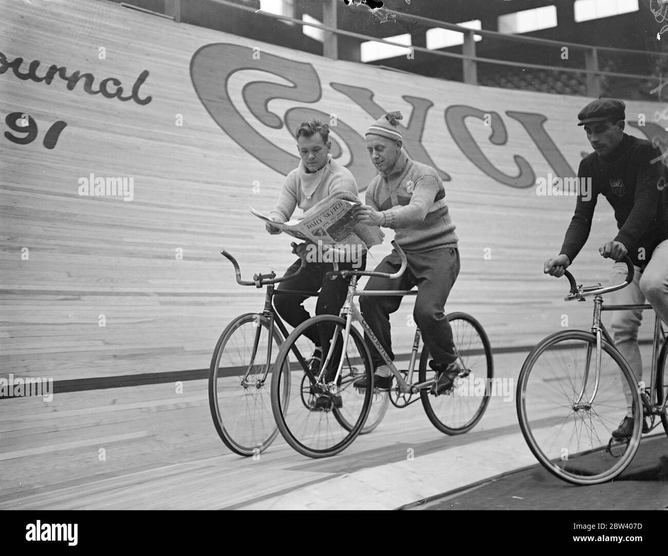 Mit den Neuigkeiten von Wembley Schritt halten . 15 Teams von Radfahrern (zwei zu einem Team) aus allen Teilen Europas kreisen Wembley Stadium in der Internationalen sechs Tage Radrennen, nur das dritte seiner Art in Großbritannien statt. Obwohl das Rennen in nur wenigen Stunden läuft, gab es bereits eine Reihe von Verletzten. Foto zeigt, Sid Cousins von Großbritannien (rechts) und J Walthour von USA (links) teilen eine Zeitung, wie sie rund um die Strecke fahren. 21. September 1936 Stockfoto