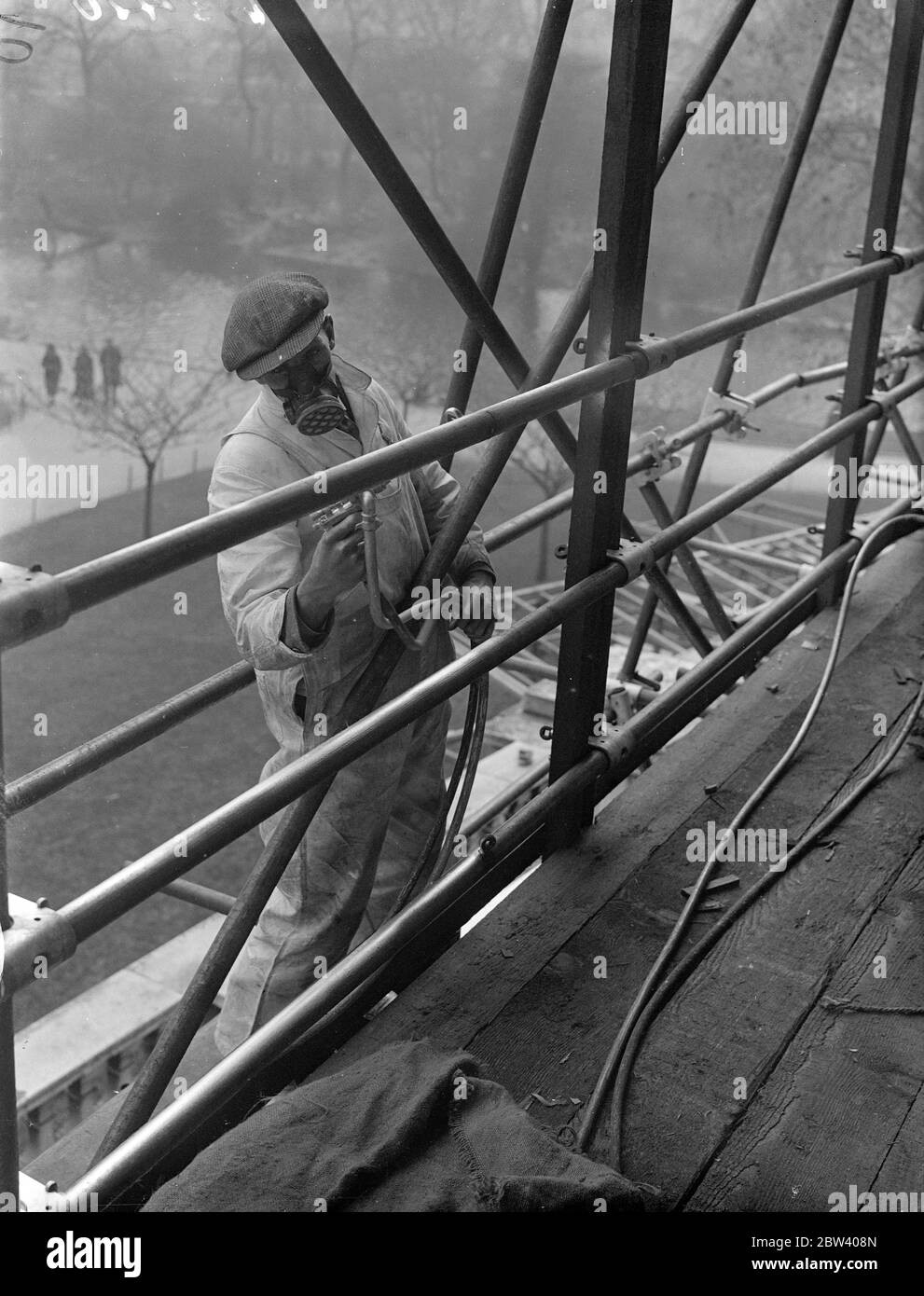 Krönungsspray von maskierten Arbeitern. Ein Arbeiter, der eine spezielle Maske trägt, während er Aluminiumfarbe auf das Stahlwerk der Krönung sprüht, steht in der Nähe des Buckingham Palace. 13. April 1937 Stockfoto