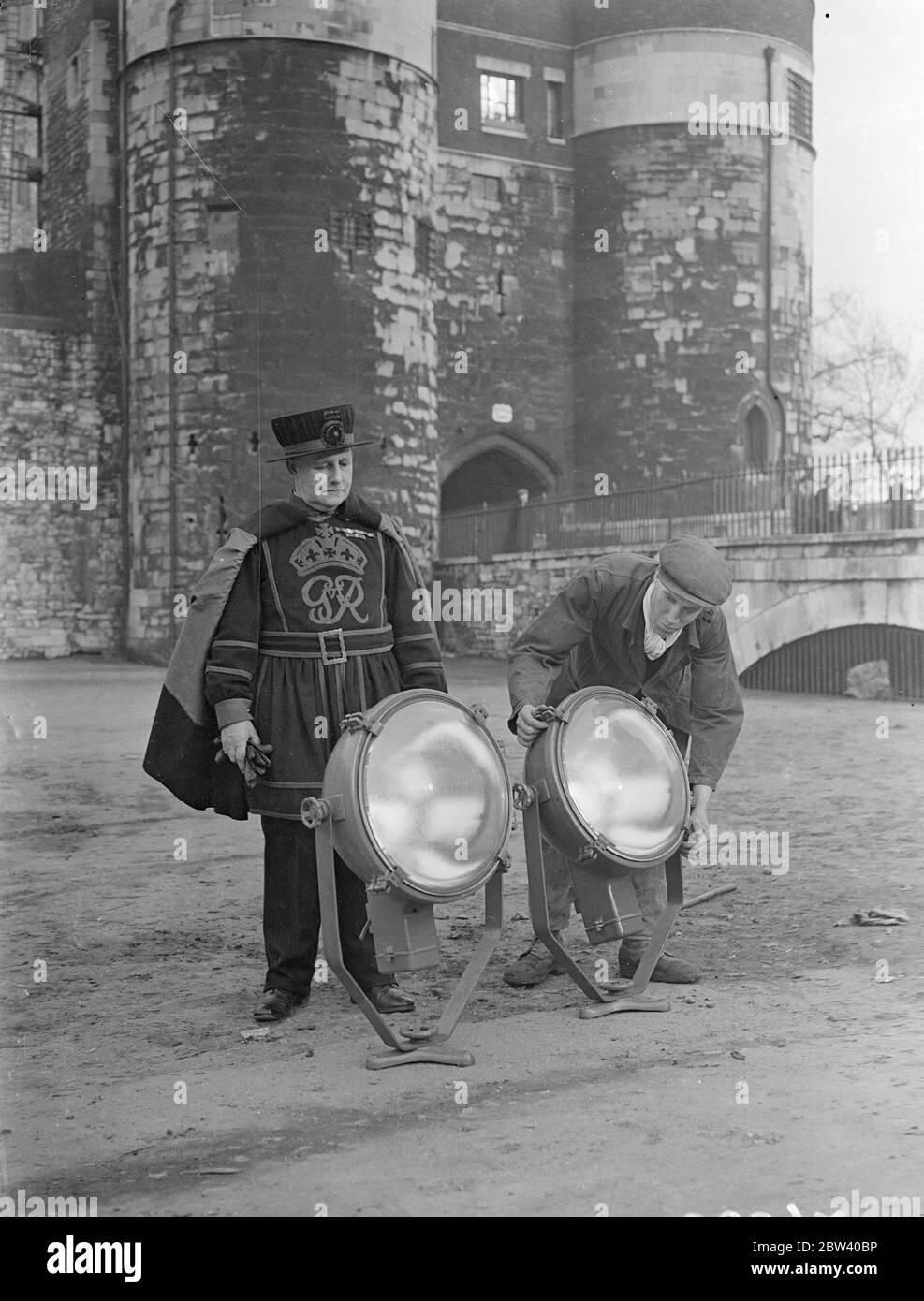 Flutlichter bei starker Krönung installiert. Am Tower of London, der zur Krönung mit Flutlicht beleuchtet werden soll, werden leistungsstarke Lampen installiert. Foto zeigt, ein Yeoman Warder beobachten die Installation der Flutlichter am Tower of London. 13. April 1937 Stockfoto