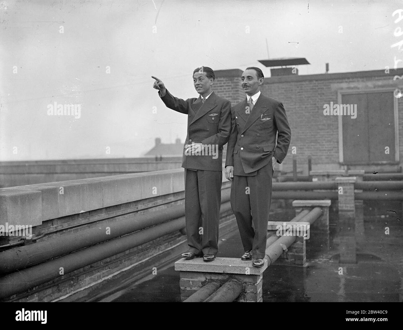 Das ist also London! Japanische Flieger schauen sich im Regen genauer an. Nachdem die japanischen Piloten Masaaki Iinuma und Kenji Tsukakoshi alle Rekorde mit dem Flug von 10,000 Meilen von Tokio nach London in gut 100 Stunden zerschlagen hatten, landeten sie Croydon in ihrem Flugzeug Divine Wind [Mitsubishi Ki-15 Karigane Aircraft, Name: Kamikaze, Registration J-BAAI]. Die Flyer haben Krönungsgrüße aus Japan mitgebracht. Foto zeigt: Die japanischen Flieger Masaaki Iinuma (links) der 27-jährige Pilot und sein Funker Kenji Tsukakoshi sehen London vom Dach ihres Hotels aus genauer. Typisches London Wetter - a s Stockfoto