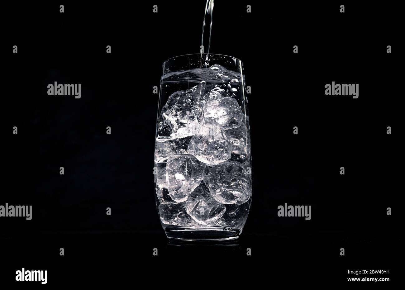 Wasser in Glas mit zerkleinertem Eis auf schwarzem Hintergrund gießen Stockfoto