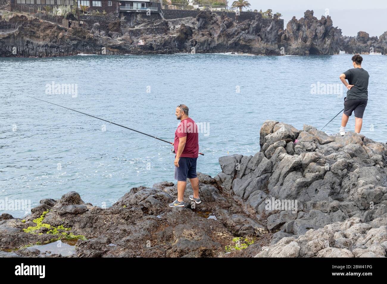 Fischer auf den Felsen am Strand mit Abschnitten, um Menschen um zwei Meter zu trennen, soziale Distanzierungsregeln, Phase zwei Deeskalation der Covid 19, Stockfoto