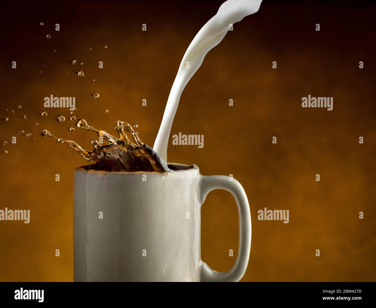 Milch wird in Kaffee gegossen, so dass Kaffee spritzt Stockfoto