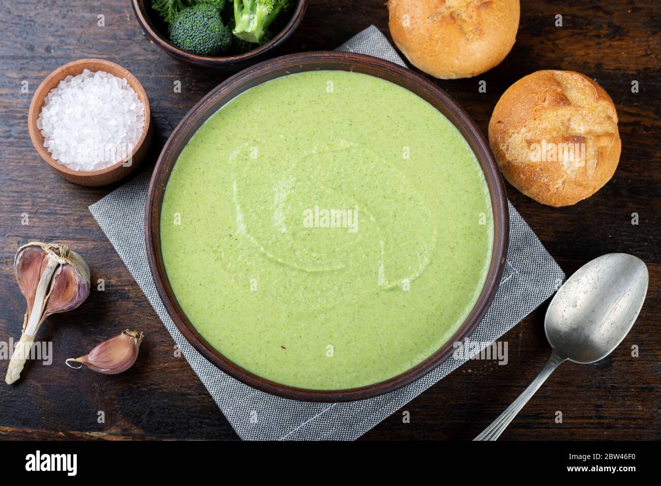 Grüne Gemüsesuppe Brokkoli in einem Teller auf dem Tisch. Daneben sind frische Brötchen und ein Blütenstand von Borkkoli Stockfoto