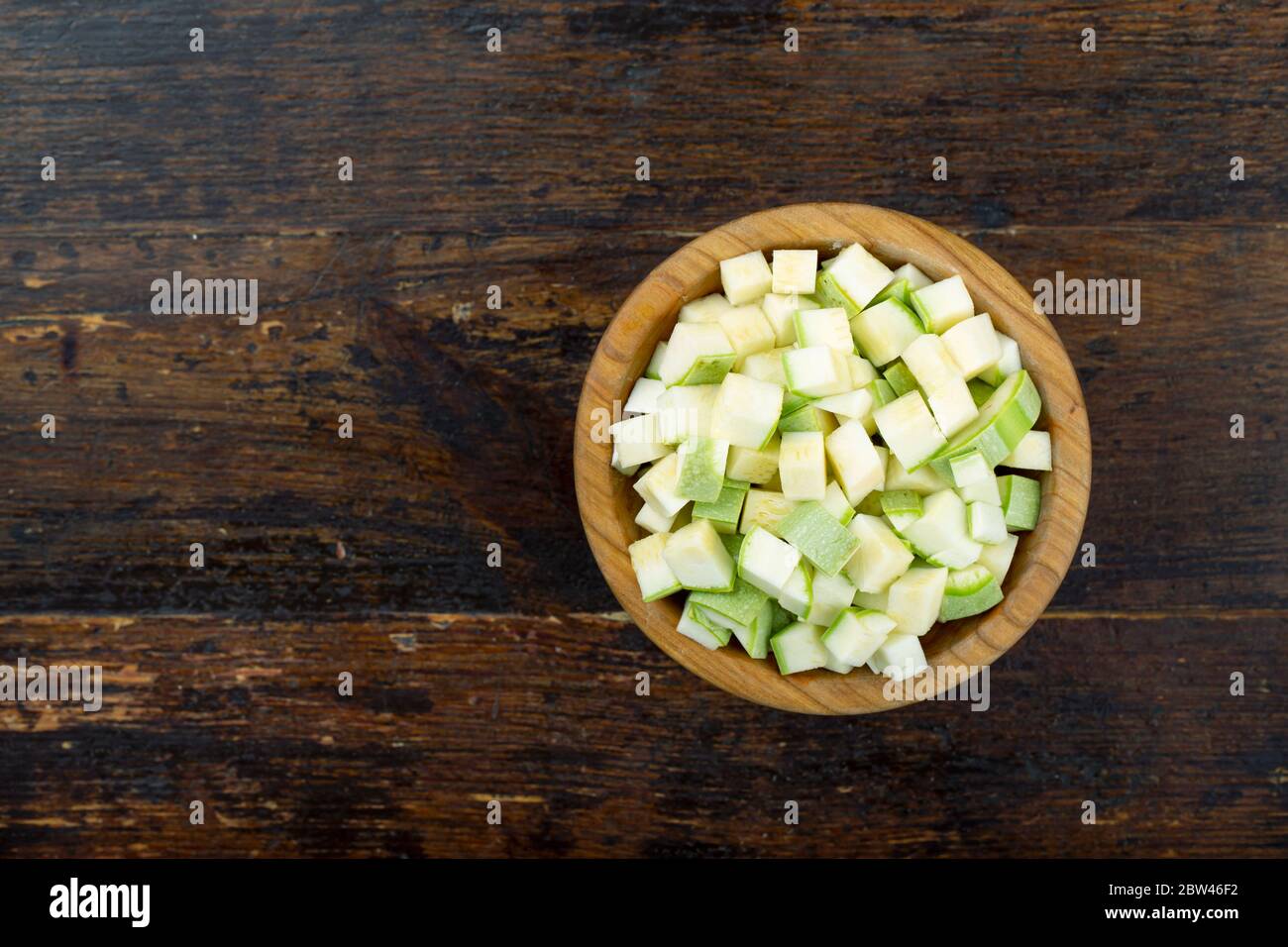 Zucchini in Würfel geschnitten in einem Holzteller auf einem braunen Holzhintergrund Stockfoto