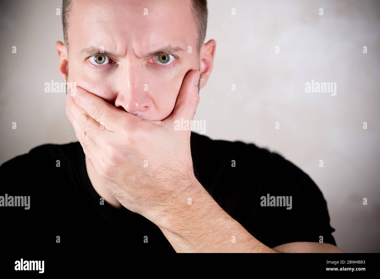 Ein Mann mit einem strengen Blick schließt seinen Mund mit Seine Handfläche Stockfoto