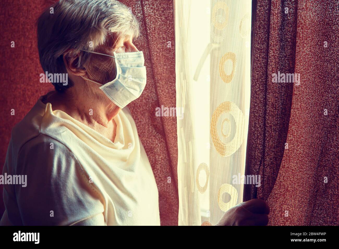 Eine ältere Frau in medizinischer Maske bleibt isoliert zu Hause für die Selbstquarantäne. Konzept Home Quarantäne, Prävention COVID-19, Stockfoto
