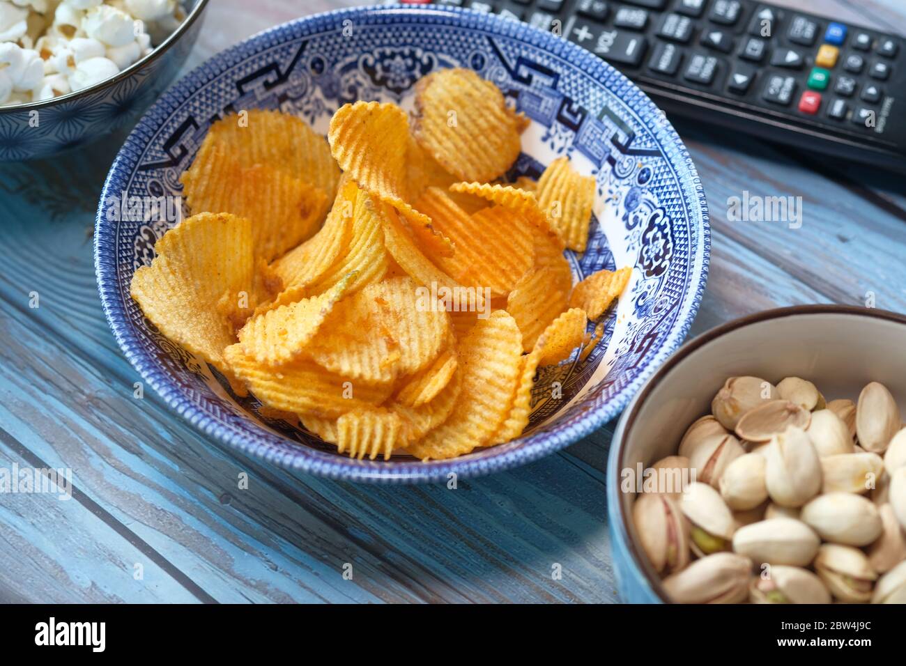 Schüssel mit leckeren Kartoffelchips, Nüssen und TV-Fernbedienung auf dem Tisch Stockfoto