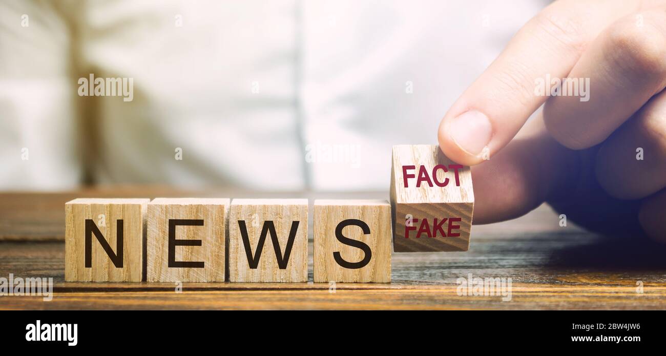 Ein Mann legt Holzblöcke mit den Worten News - Fakt oder Fake. Falsches / wahres Informationskonzept. Gelbe Drucktaste. Stockfoto