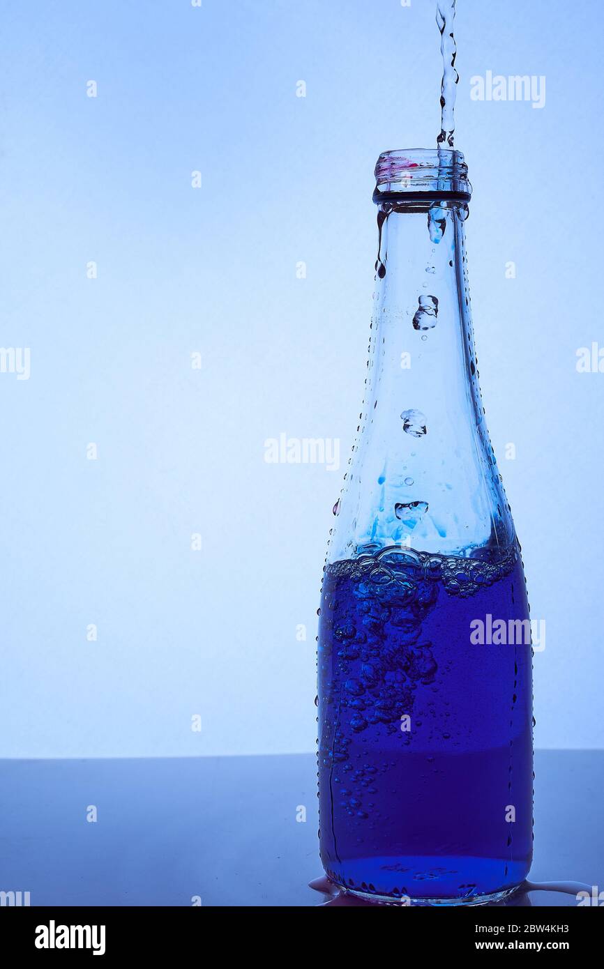 Eine blaue Flüssigkeit wird in eine Glasflasche gegossen. Hellblauer Hintergrund Stockfoto
