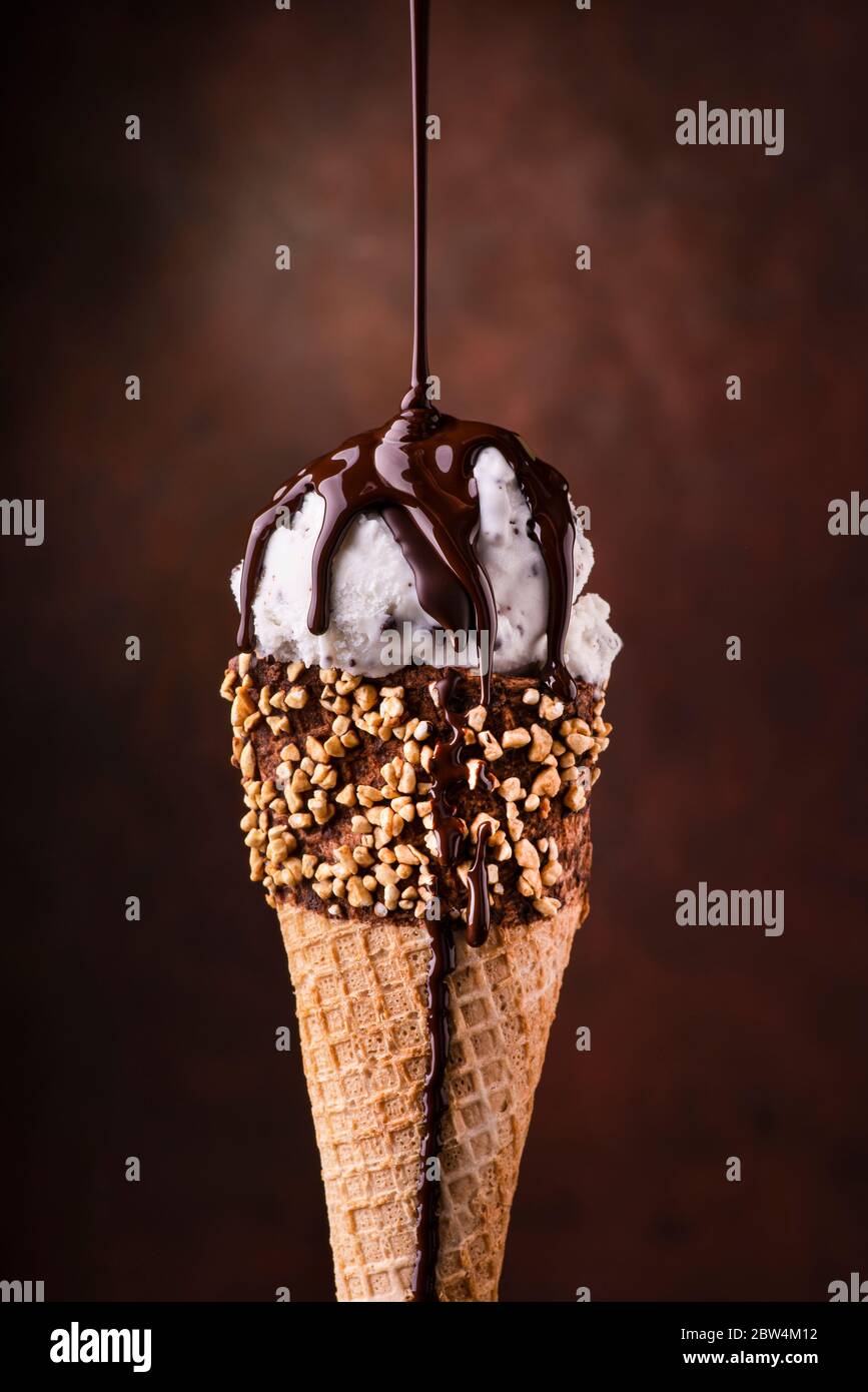 Eiscreme mit Tropfen geschmolzener dunkler Schokolade und gehackten Haselnüssen Stockfoto