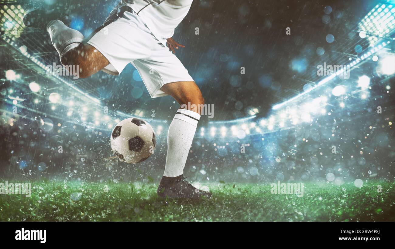 Nahaufnahme einer Fußballszene bei einem Nachtspiel mit dem Spieler in einer weißen Uniform, der den Ball mit Macht in die Höhe leitet Stockfoto
