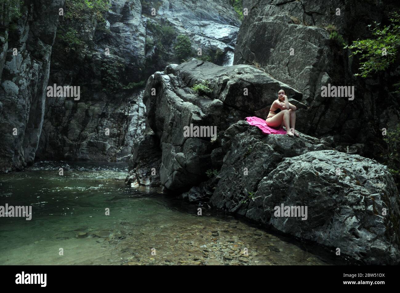 Eine griechische Frau, die auf einem Felsen nahe einem Wasserfall auf dem Fonias Fluß sitzt, auf der nordgriechischen Insel Samothraki, Nordägäis, Thrakien, Griechenland. Stockfoto