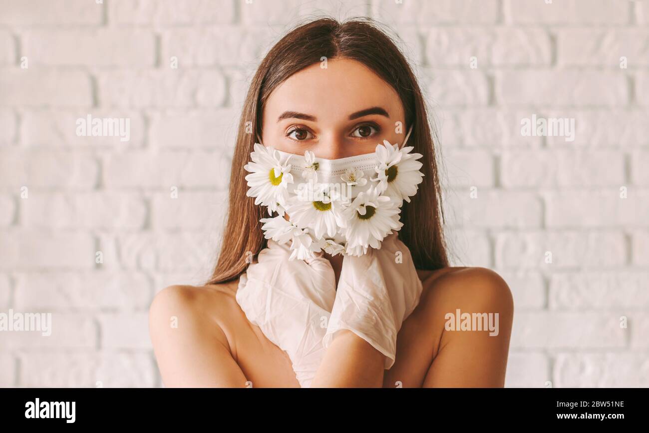 Portrait junge zärtliche Frau posiert in Schutzhandschuhen und Sommer medizinische Gesichtsmaske. Schöne zarte Mädchen tragen Schutzmaske mit fl Stockfoto