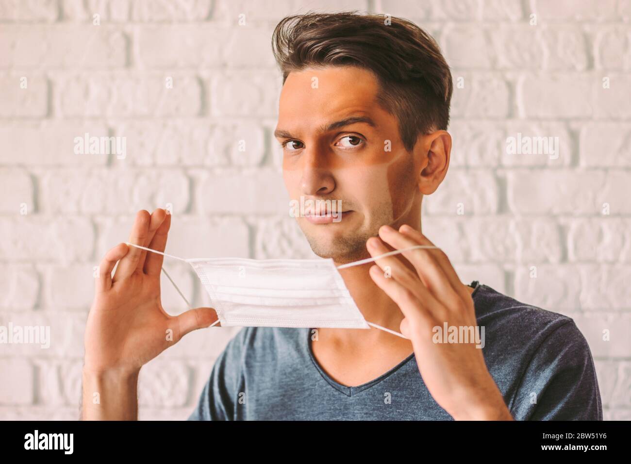 Porträt von verwirrt wütend Mann Patient mit lustigen Sonne tan Linien im Gesicht tragen Schutzmaske. Junge Hipster Mann mit Sonnenbrand gebräunte Haut aus Stockfoto