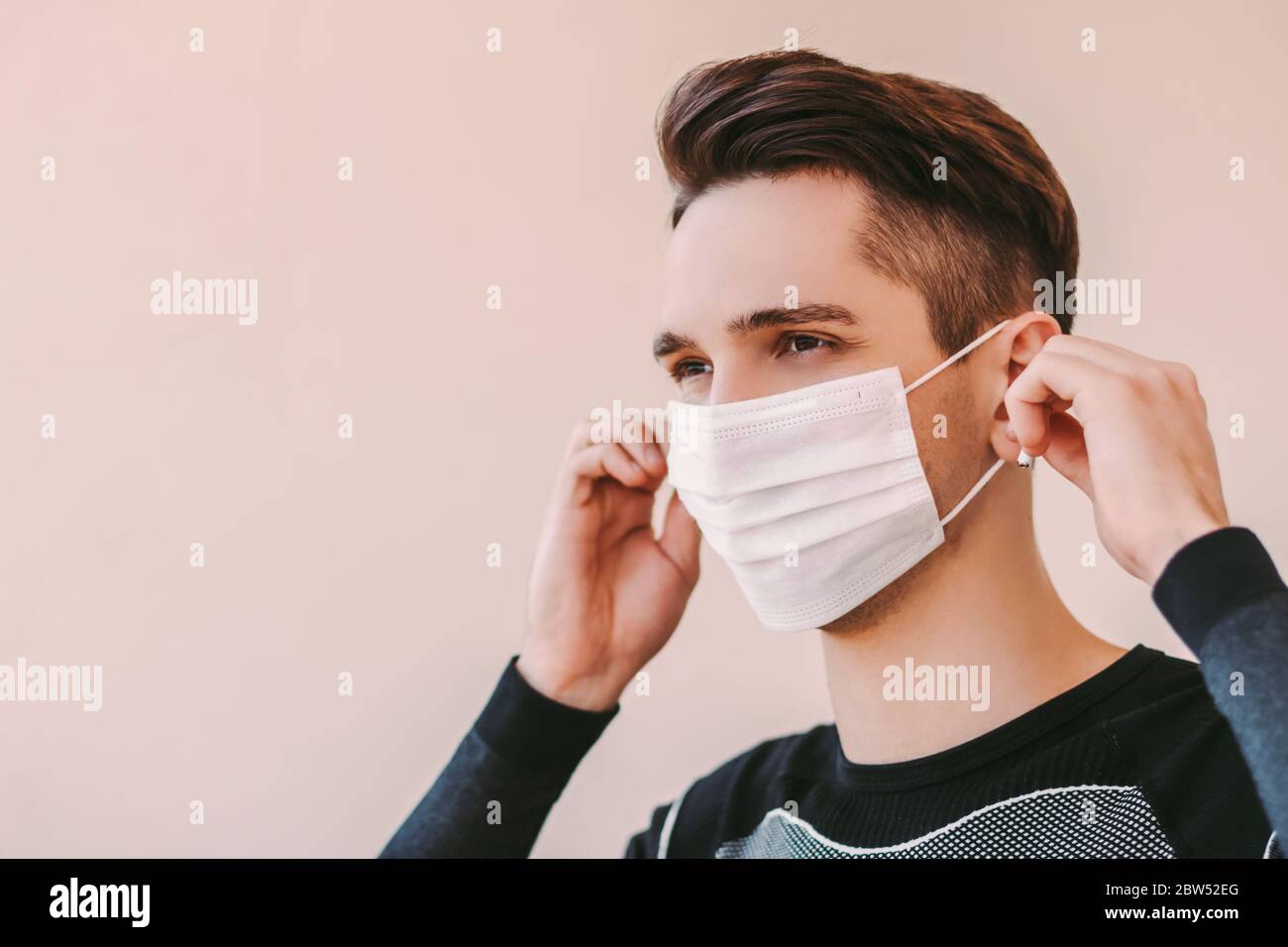 Selbstbewusster Sportmann in medizinischer Gesichtsmaske hört Musik mit kabellosen bluetooth-Kopfhörern. Happy Fitness-Trainer in Schutzmaske trägt Ohrstöpsel. Stockfoto