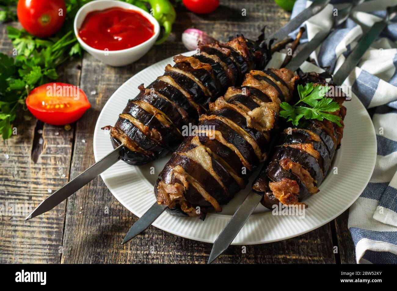 Barbecue-Menü im Sommer. Gegrillte Aubergine mit Speck auf rustikalem Holztisch. Stockfoto