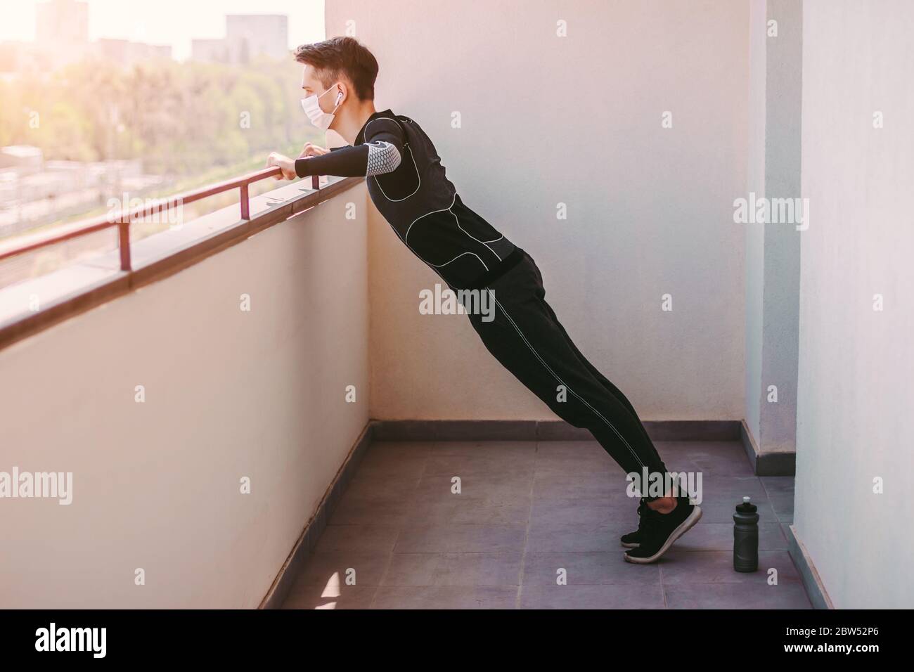 Junge sportliche Sportman in schützende Gesichtsmaske tun Liegestützen Übungen zu Hause. Sportlich selbstbewusster Fitness-Mann im medizinischen Gesichtsmaske Training Workout Stockfoto