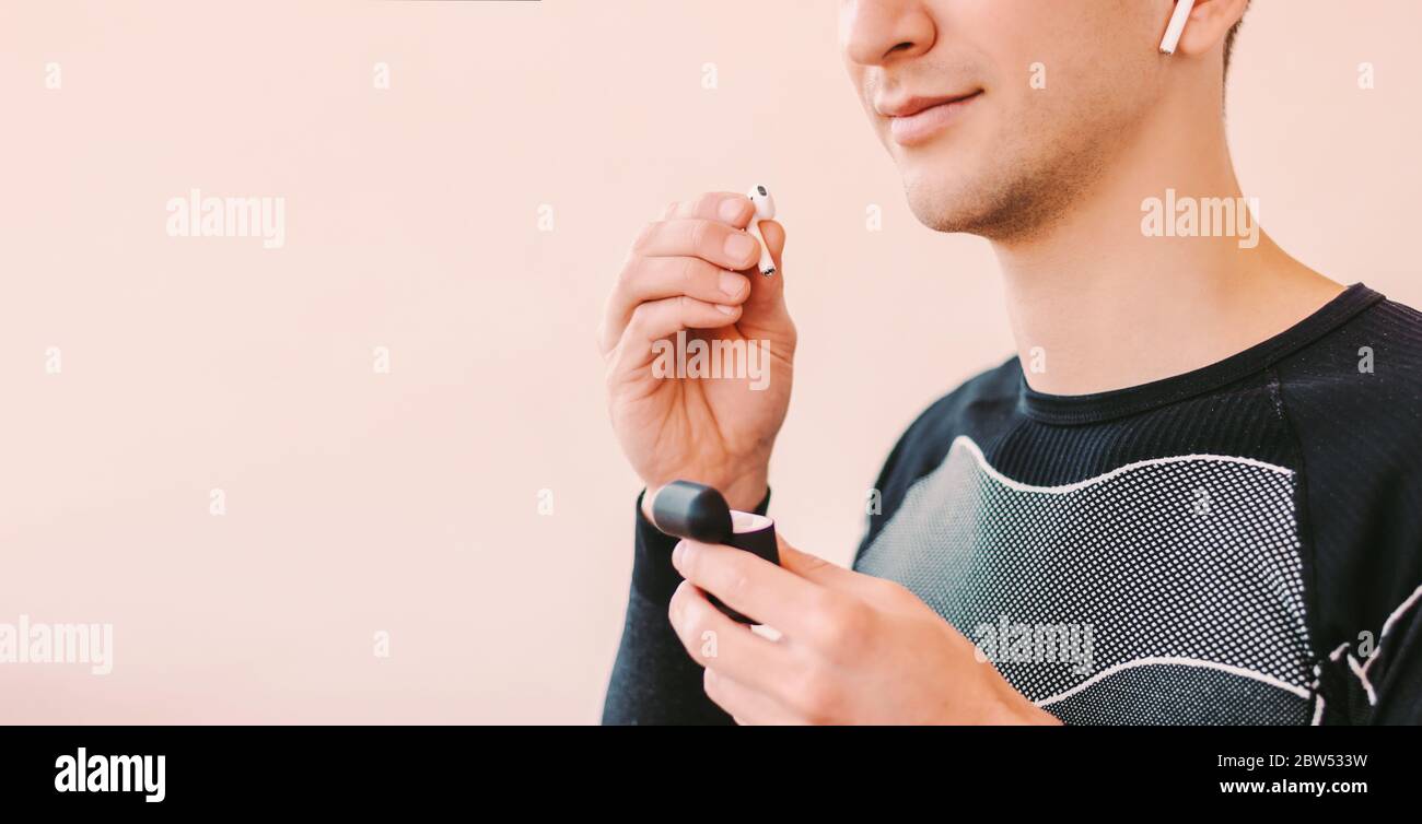 Nahaufnahme eines glücklichen Sportmanns, der Bluetooth-Kopfhörer ins Ohr legt und vor dem Hintergrund lächelt und mit Kopierfläche lachend ist. Junger Fitness-Mann Musik in w Stockfoto