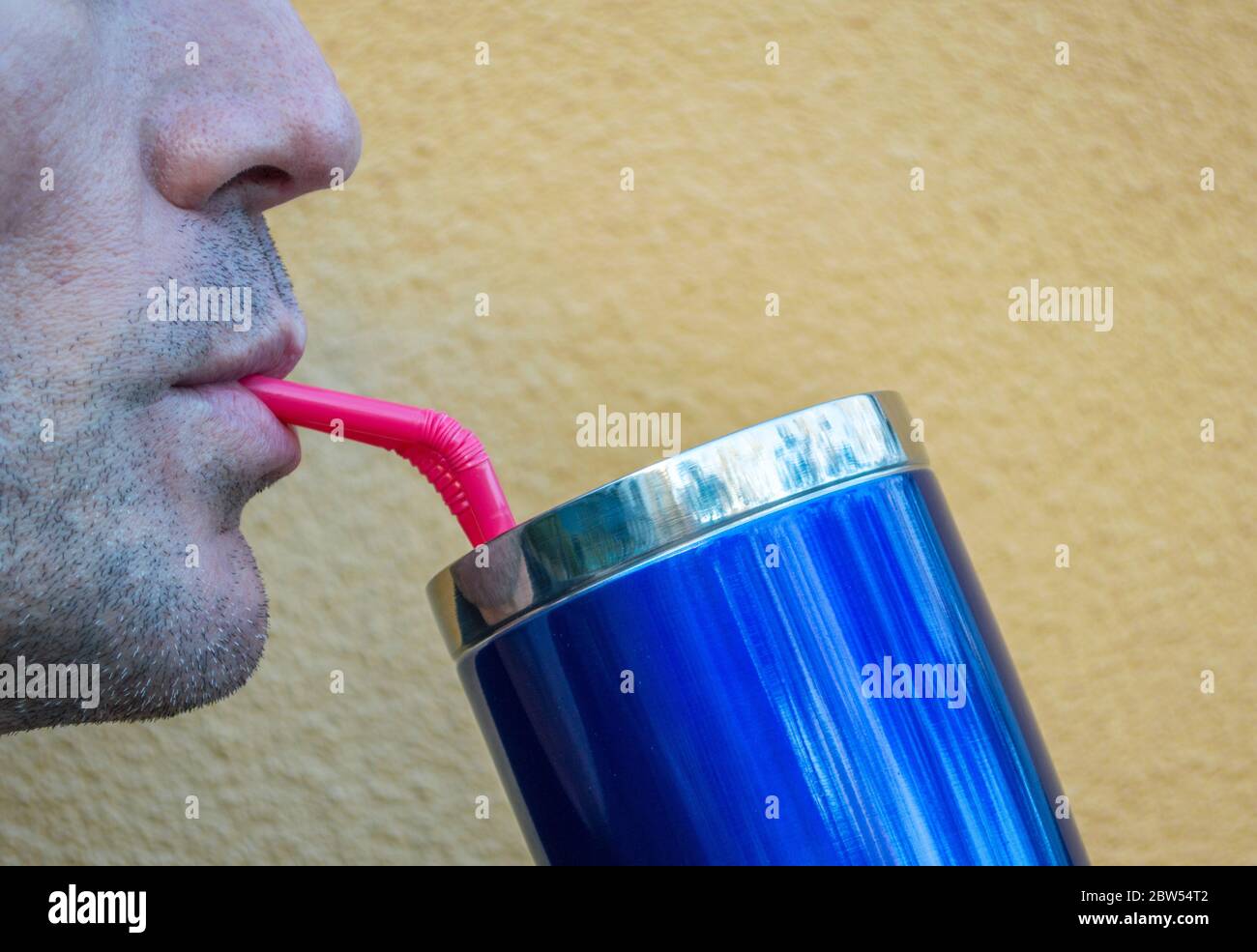 Nahaufnahme des Profils eines kaukasischen Mannes Nase und Mund, während er aus einem glänzend blauen Tasse durch ein rosa Stroh mit Kopie Raum schlürft Stockfoto