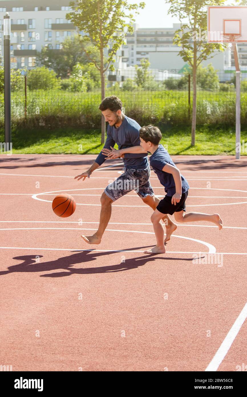 Vater und Sohn spielen barfuß Basketball mit dem Ball auf einem Spielplatz Stockfoto