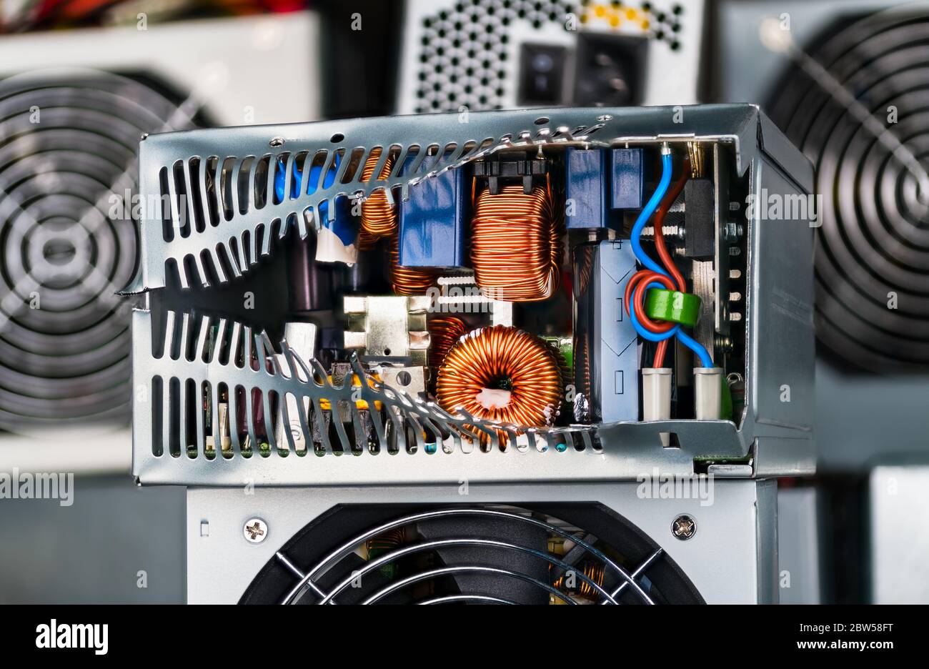 Entsorgung von Elektroschrott. Elektronische Komponenten im beschädigten Netzteilkasten. Ringspulen mit Kupferdrahtwicklung, Kondensatoren und Drossel. Stockfoto