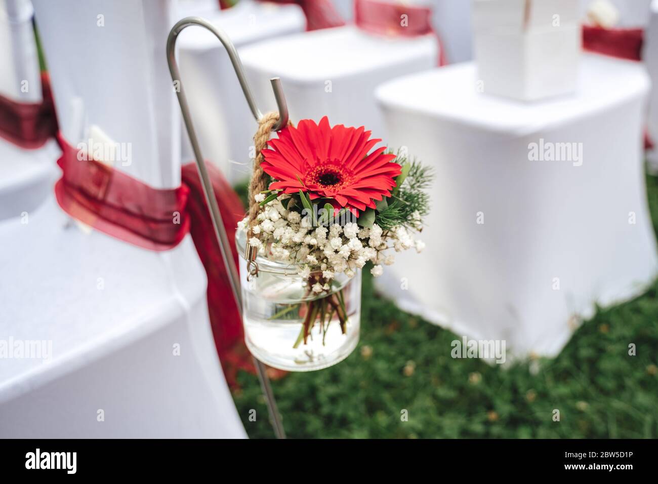 Hochzeitsdeko mit Blumenmuster. Rote Gerbera Blume in Glasvase. Outdoor-NUPTials. Konzept für Hochzeitstag. Stockfoto