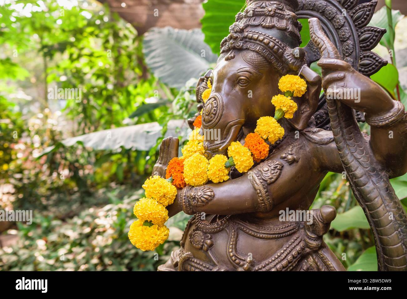 Bronze Ganesha Statue mit Ringelblumen im tropischen Garten Stockfoto