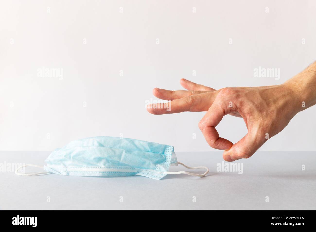 Nahaufnahme der Hand des Mannes wird von gebrauchten blauen chirurgischen Schutzmaske, weißen Hintergrund loszuwerden. Kopierbereich. Ende der Quarantäne, Ausbruch von Covid-19. Stockfoto