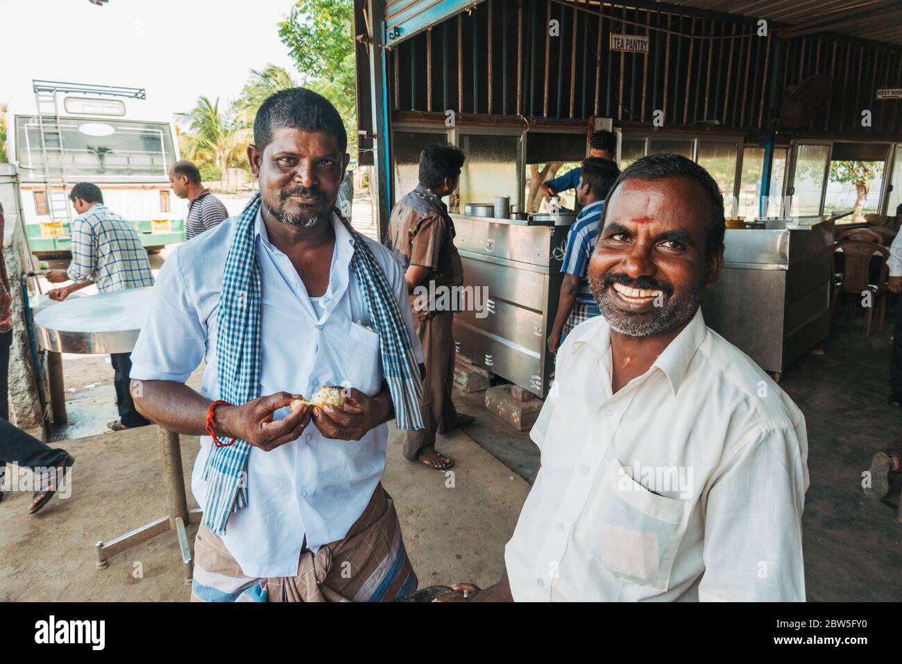 Zwei indische Männer lächeln an einer Bushaltestelle in Tamil Nadu, Indien, zur Kamera Stockfoto