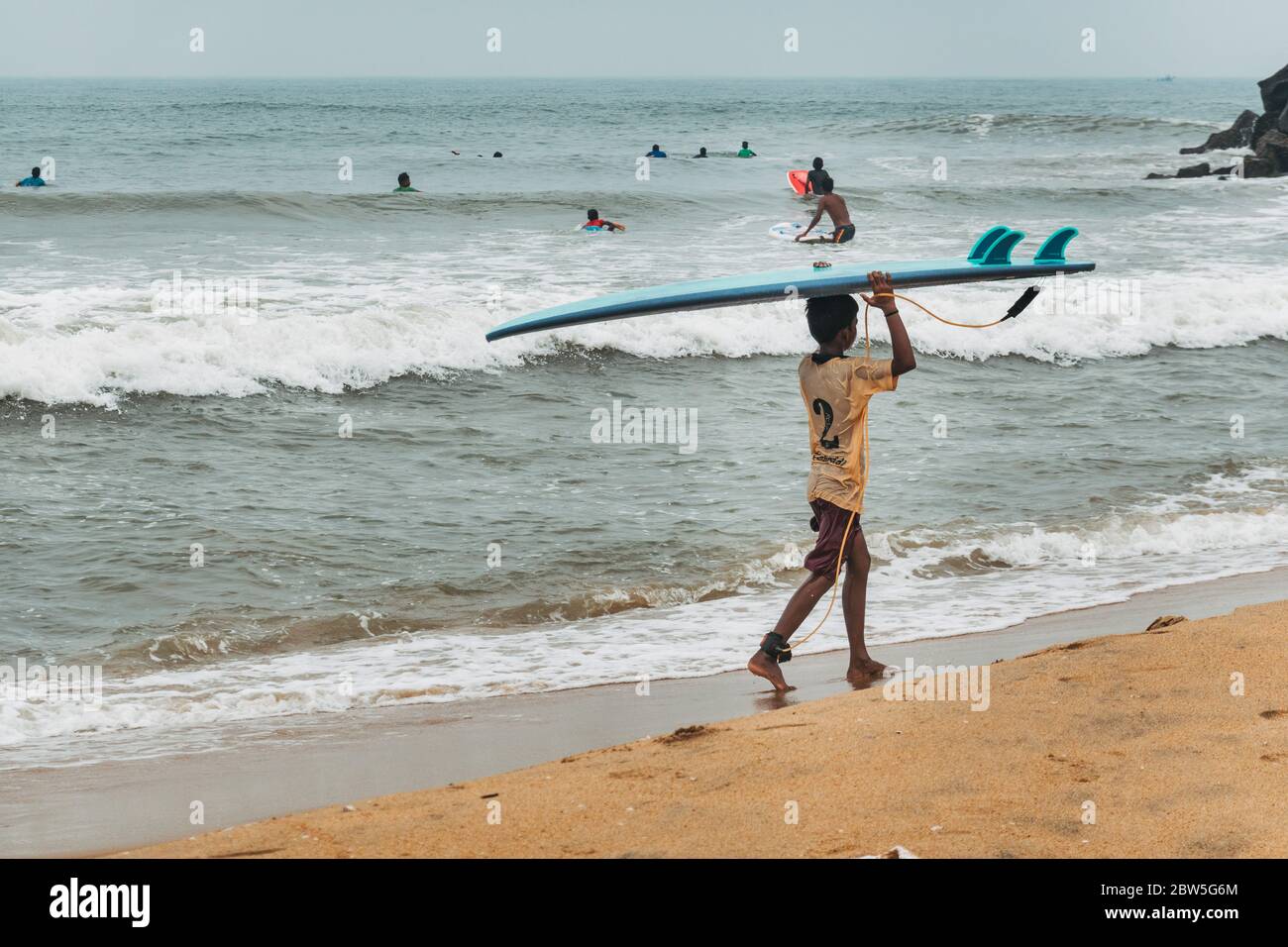 Ein kleiner indischer Junge trägt ein Surfbrett auf seinem Kopf am Mahabalipuram Beach, Tamil Nadu, Indien Stockfoto