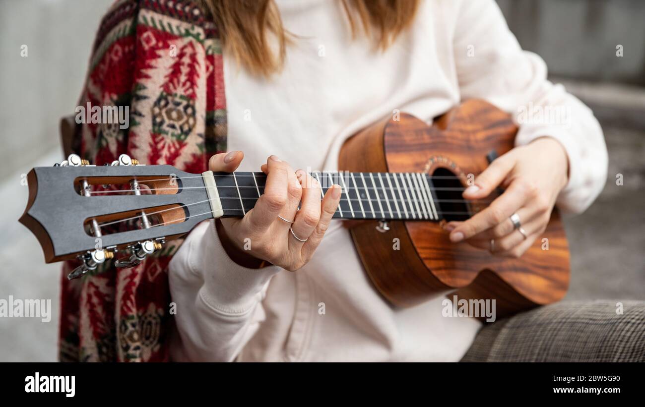 Frau spielt hawaiianische Gitarre, singt ein Lied auf vintage Ukulele zu Hause. Selektiver Fokus. Nahaufnahme. Stockfoto