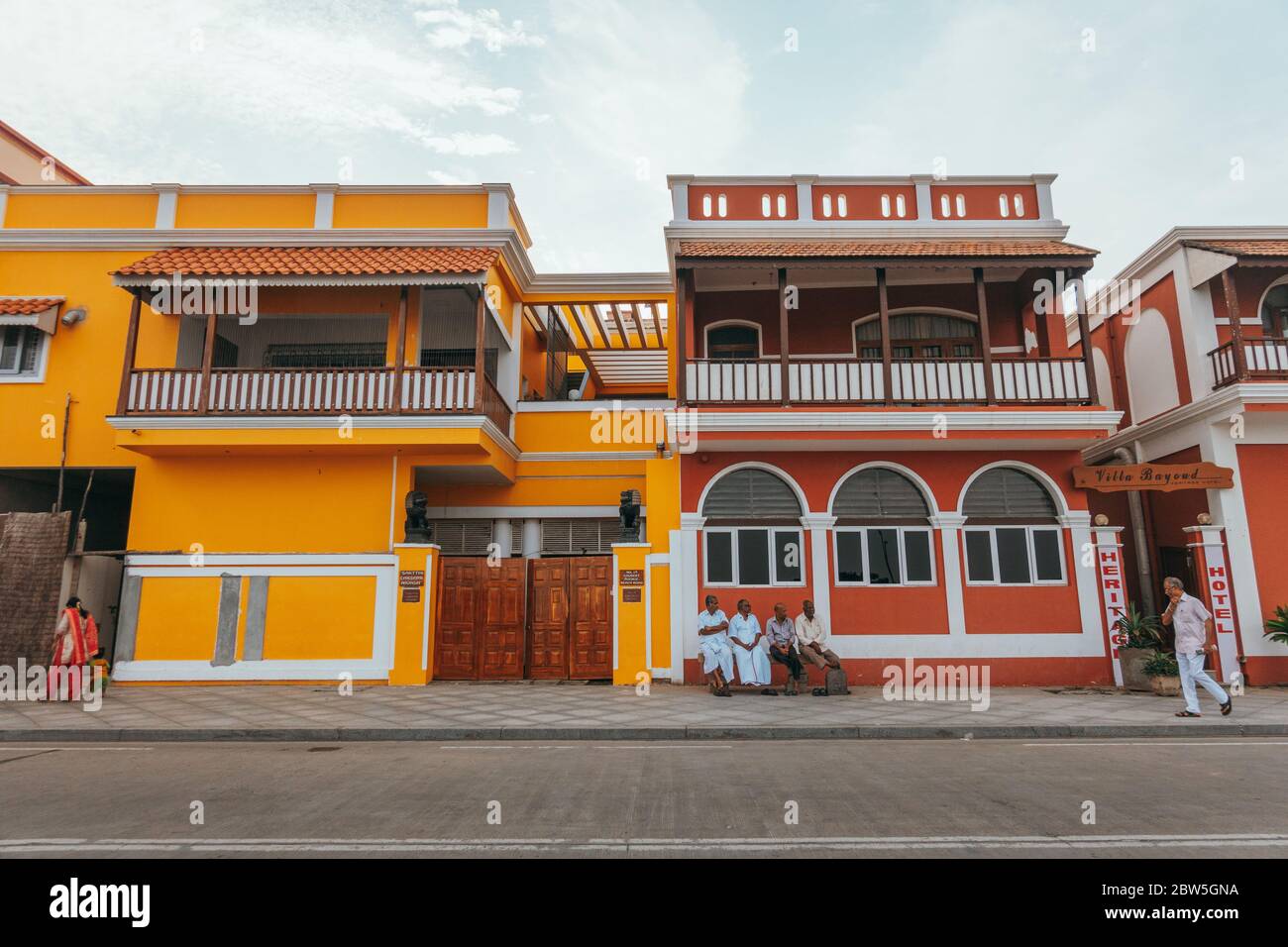 Vier Männer sitzen auf einer Bank vor bunten Gebäuden aus der französischen Kolonialzeit in White Town, Pondicherry, Indien Stockfoto