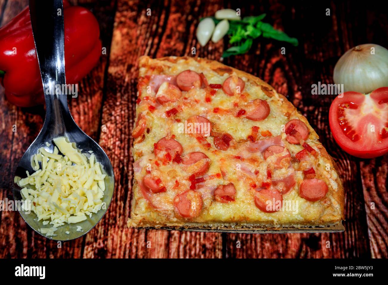 Nahaufnahme von Wurst, Schinken, Salami und Käse Pizza Scheibe auf dunklem Holzhintergrund mit frischen Zutaten Stockfoto