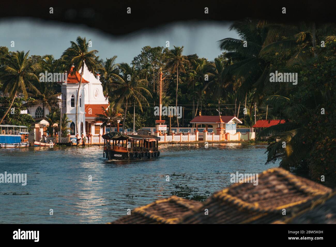 Ein Hausboot treibt an einer kleinen christlichen Kirche am Ufer des Kerala-Hinterwassers in Indien vorbei Stockfoto