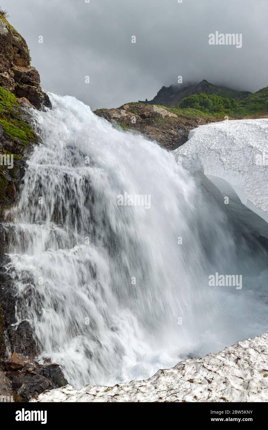 Blick auf die Landschaft des idyllischen Wasserfall Wasserfall fallen in Schneefeld in felsigen Mount Stockfoto