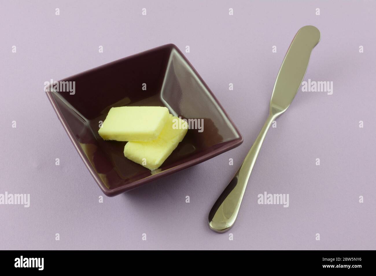 Zwei Pats Butter in lila Butterform mit Buttermesser auf Lavendelhintergrund Stockfoto