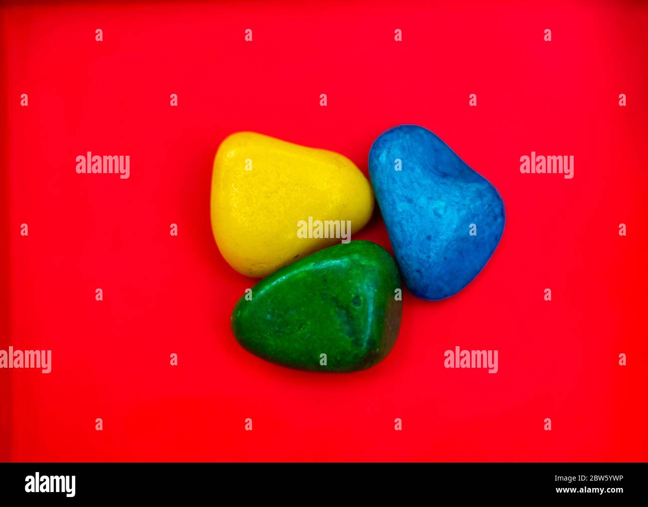 Multi Color natürliche Kieselsteine Grün, Blau und Gelb Stein isoliert auf rotem Hintergrund mit Platz für Text und Wörter kopieren. Bunte Natursteinsteine Stein Stockfoto