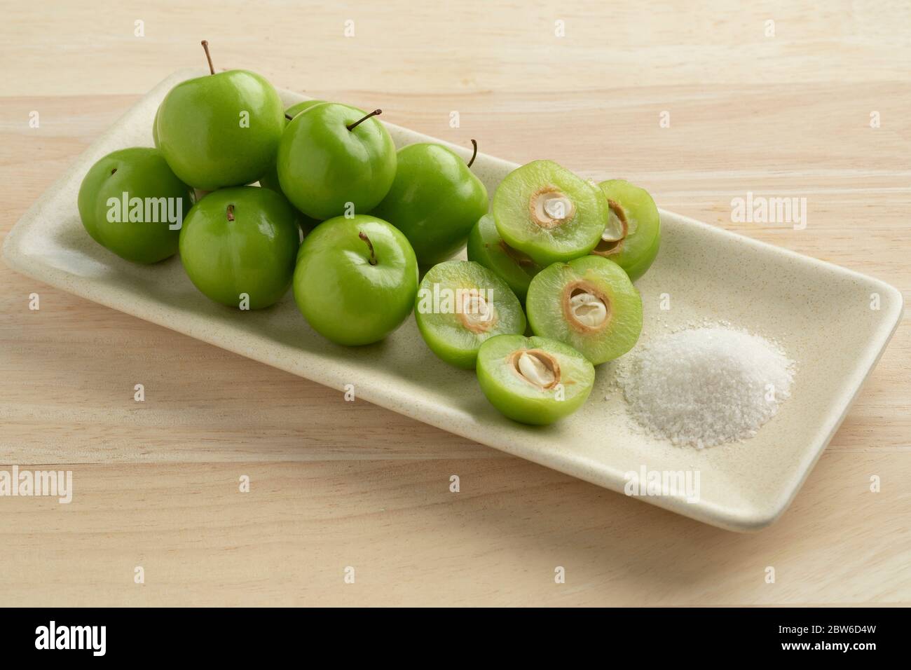 Gericht mit frischen grünen ganzen und Hälfte Dose Erik Pflaumen und eine Schüssel mit Salz Stockfoto